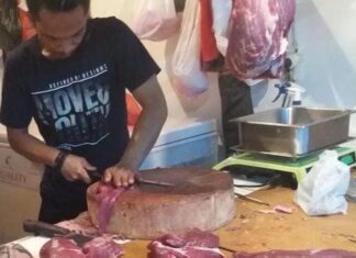 Seorang pedagang daging sapi sedang memotong daging per bagian